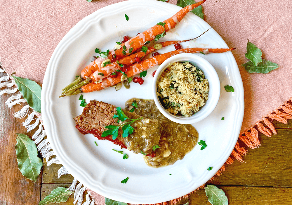This image shows a completely plant-based meal that is very similar to a standard American dinner. It has plant-based meatloaf, mushroom gravy, roasted carrots, and a creamy kale gratin.