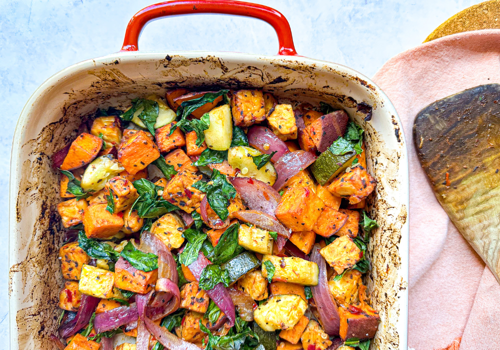 This image shows a closeup of a plant-based breakfast hash in a red and white baking dish with an orange napkin.